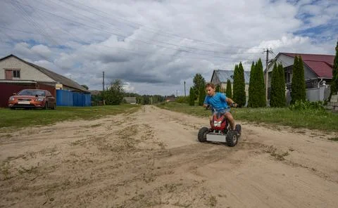A child makes a sharp turn on an ATV, kicking up dust and sand from the road Stock Photos