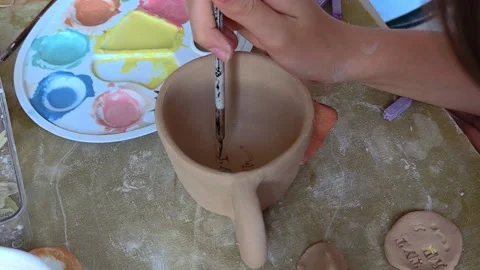Child making creative clay cups and bowls at table in pottery workshop. Video stock 291627868