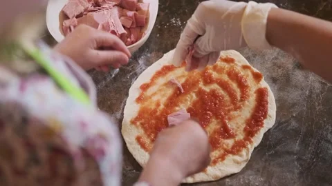 Child making pizza by the table in kitchen. Little girl putting ham on a dough 스톡 동영상 139398953