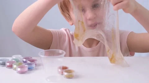 The child mixes two colors of sequins in a slime and admires the result Stock Footage 169689790