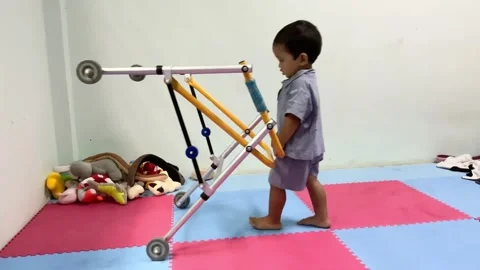 Child with a mobility aid practicing walking in a therapy room Видео 341498497
