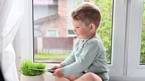 The child mows the grass with scissors. sitting on the windowsill Stock Footage 131594331