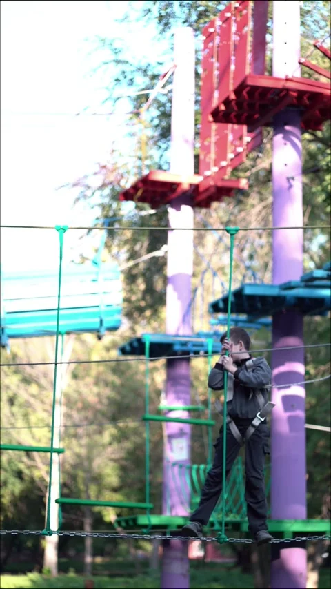 Child navigates a high ropes course with hanging green platforms and cables Stock Footage 345285585