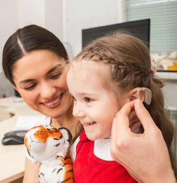 Child is not afraid that she needs to use a hearing aid on her ear. Mother of 스톡 사진