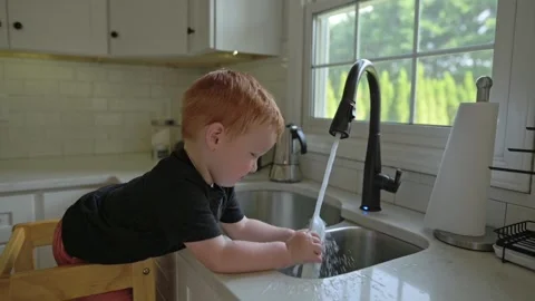 Child observing water, young boy focusing on flowing water stream, redheaded Vidéo 323096152
