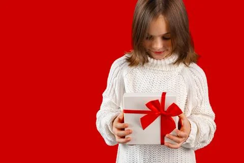 Child opening gift box with red ribbon and looking inside with curiosity on red Stock Photos