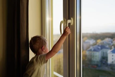 Child opening window without parents. Dangerous situation Stock Photos