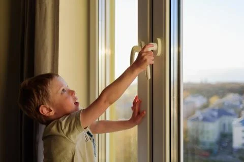Child opening window without parents. Dangerous situation Stock Photos