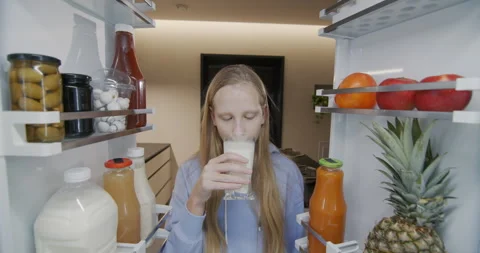 The child opens the refrigerator and drinks milk from a glass. Snack on the go Stock Footage 263973609