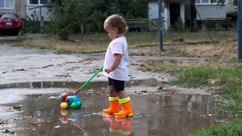 A child in orange boots pulls a toy and walks through the puddles. Stock Footage 138167813
