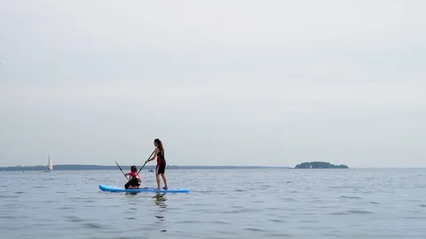 A child at a paddleboard class with an open water coach on a sunny day. Stock Footage 123648512