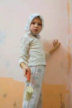 Child painting a wall while standing on a small chair in a room during the da Stock Photos