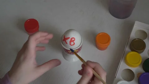 The child paints Easter egg colors and draws symbols on it with a brush. Close Stock Footage 103094647