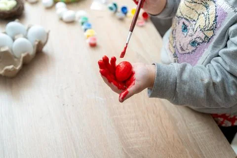 Child paints easter egg red with a brush in celebration of the Spring holiday Stock Photos