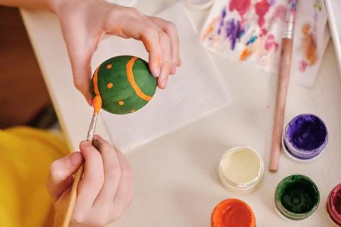 A child paints Easter eggs with paints. Hands paint an Easter wooden egg with Stock Photos