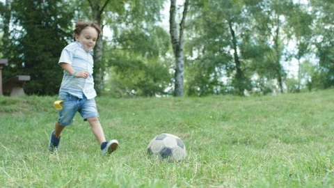A child at the park kicks a ball on the side of the camera staring if he scores 库存影片 98561673