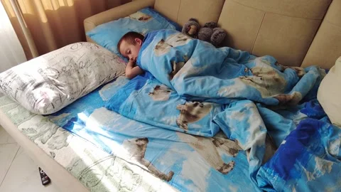 A child is peacefully sleeping on a couch adorned with blue bedding, nestled in Stock Footage 344517852