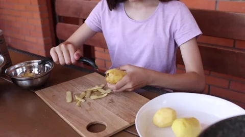 Child peels potatoes at kitchen table in rustic cooking space Stock Footage 297358607
