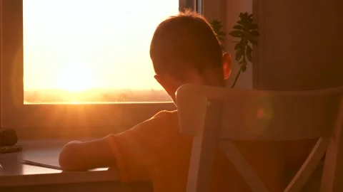 Child pens notes at sunset writes in album near window sunset Stock Footage 326046947