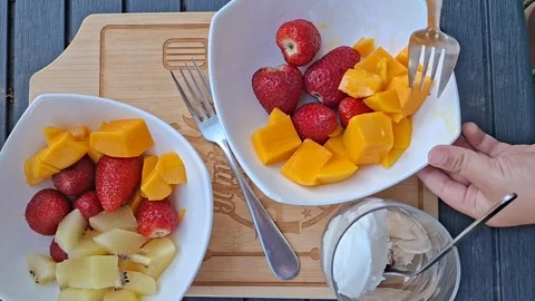 Child Picking Up Slippery Mango Slice with Fork from Fruit Bowl, Top View 스톡 동영상 334699173