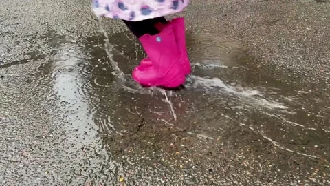 A child in pink  boots is jumping on a puddle Stock Footage 160032103