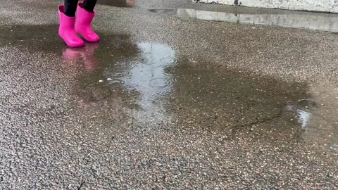 A child in pink  boots is jumping on a puddle Stock Footage 162018275