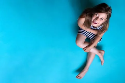 Child on plain blue background looking at camera sitting 스톡 사진