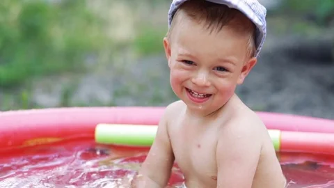 Child play and having fun in inflatable rubber pool of green lawn on a sunny day Stock Footage 77804696