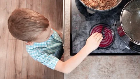 Toddler boy touches hot stove in kitchen. Accident at home with children.  Child pulls a hand to a scorching pan Stock Photo