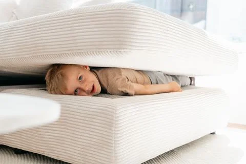Child Playfully Hides Between Sofa Cushions at Home Foto stock