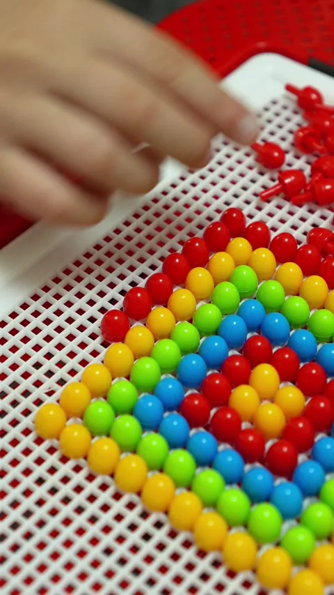 The child is playing and inserting red parts into the mosaic constructor. Close- Stock Footage 317918026