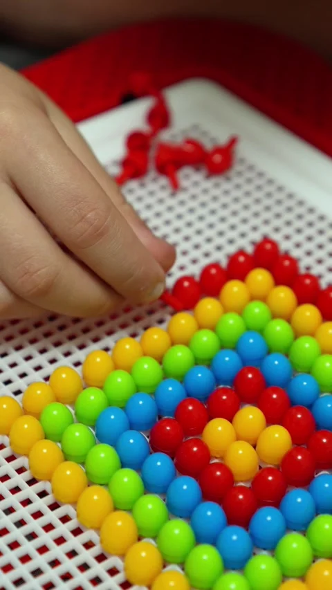 The child is playing and inserting red parts into the mosaic constructor. Close- Stock Footage 317918129