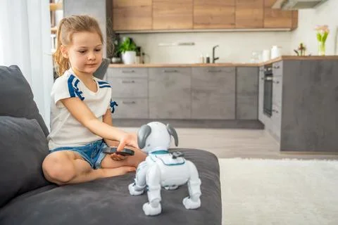 Child playing and interacting with robotic dog on sofa at home. Human robot Stock Photos