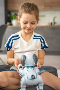 Child playing and interacting with robotic dog on sofa at home. Human robot Stock Photos