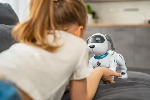 Child playing and interacting with robotic dog on sofa at home. Human robot Stock Photos