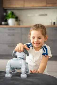 Child playing and interacting with robotic dog on sofa at home. Human robot Stock Photos