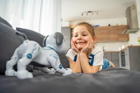 Child playing and interacting with robotic dog on sofa at home. Human robot Stock Photos