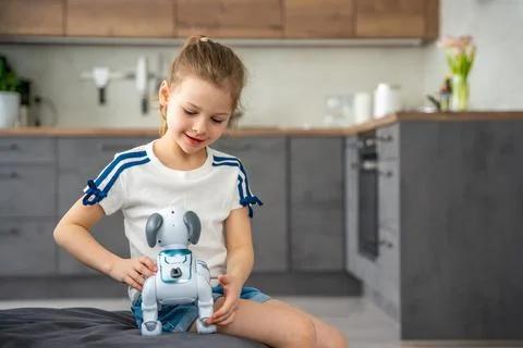 Child playing and interacting with robotic dog on sofa at home. Human robot Stock Photos