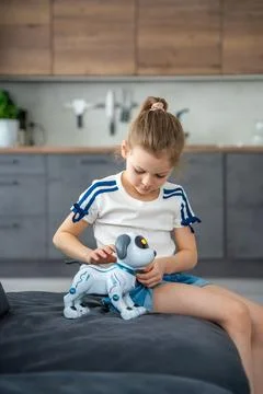 Child playing and interacting with robotic dog on sofa at home. Human robot Stock Photos