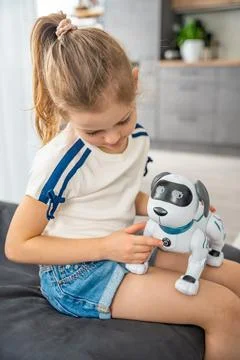 Child playing and interacting with robotic dog on sofa at home. Human robot Stock Photos