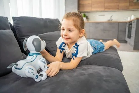 Child playing and interacting with robotic dog on sofa at home. Human robot Stock Photos