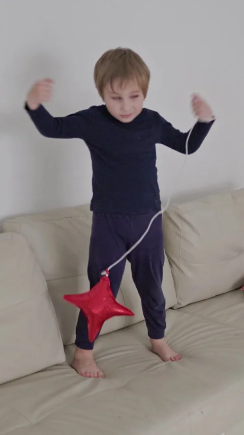 Child playing and jumping on sofa with red balloon Stock Footage 327042295