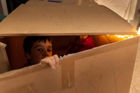 Child playing and looking through the crack of a cardboard box Stock Photos