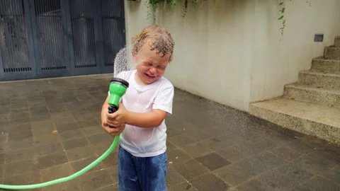 Child playing and spraying water on his face with garden hose Stock Footage 310299573
