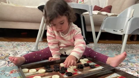 Child playing with backgammon stones sitting on the ground Stockbeeldmateriaal 272321084