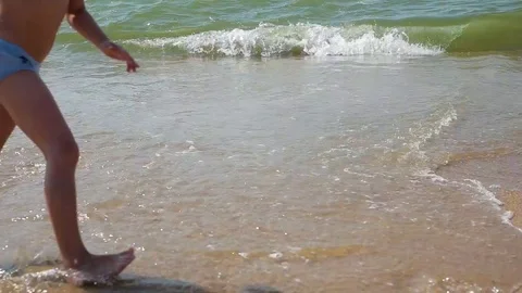 Child playing on a beach. Kid jumping in the waves. Sea vacation for family with Stock Footage 113819928