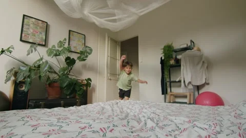 Child playing on the bed and jumping around like superman in the bedroom Stock Footage 287189797