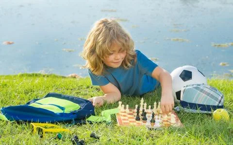 Child playing chess game in spring backyard, laying on grass. Concentrated kid Stock Photos
