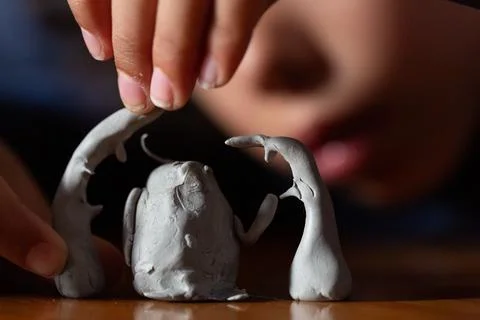 Child playing with clay creating imaginary characters on a wooden table Stockfoto's