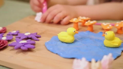 Child playing with clay ducks and flowers on a wooden board Stock Footage 311437565